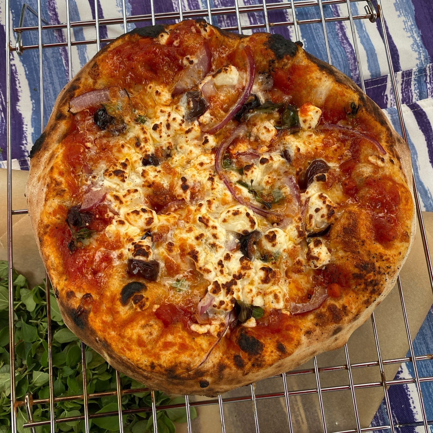 Small pizza on a cooling rack on a blue and white striped tablecloth.