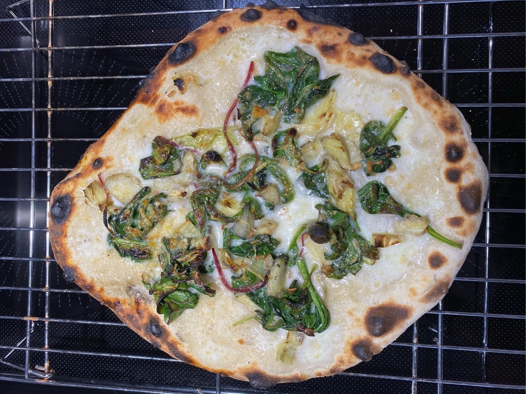 Small white pizza on a cooling rack.