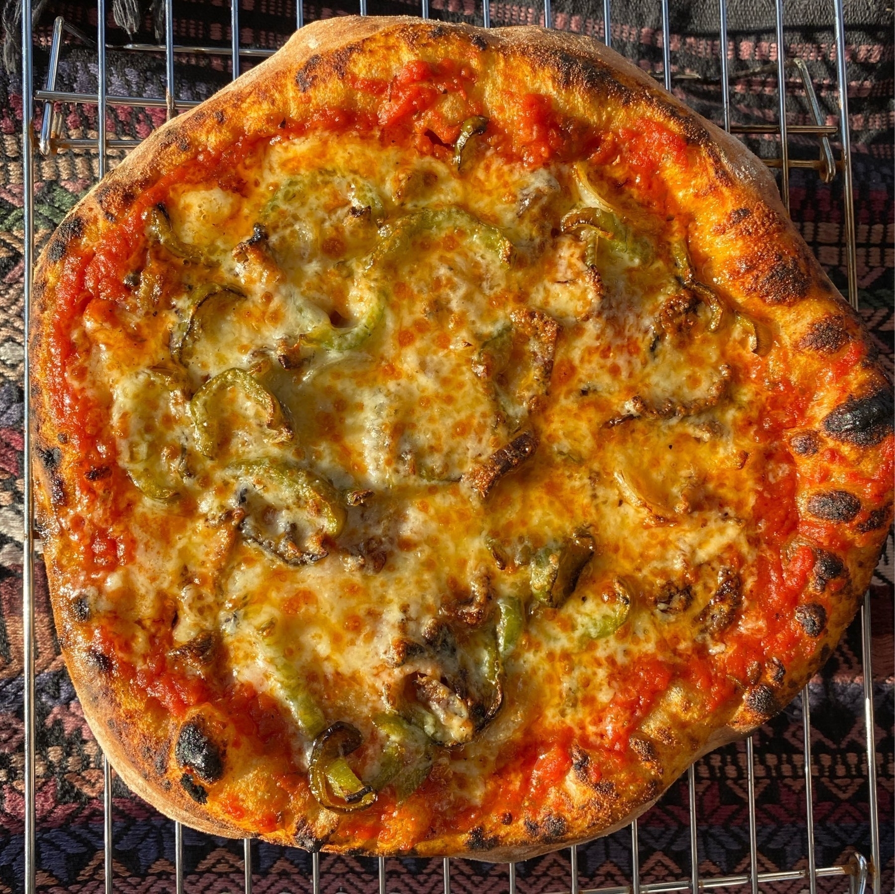 Small pizza on a cooling rack, sitting on a table with a dark tablecloth.