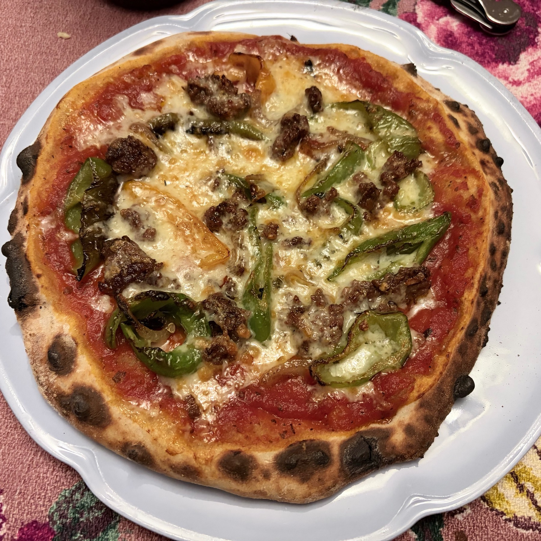 Close up view of a small pizza on a light blue plate, sitting on a purple and pink table cloth.