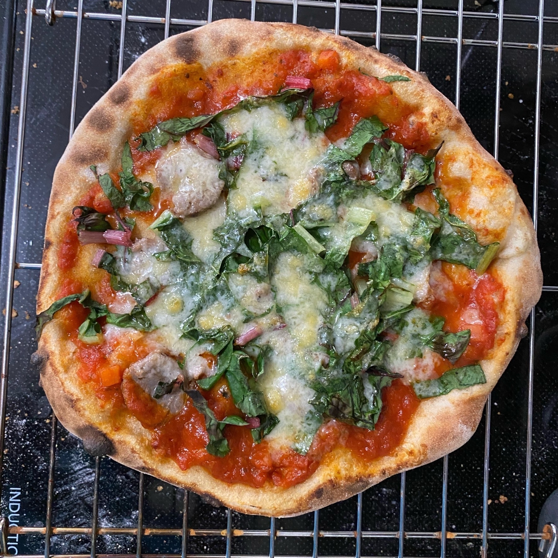 A small pizza on a cooling rack sitting on a black stove top.