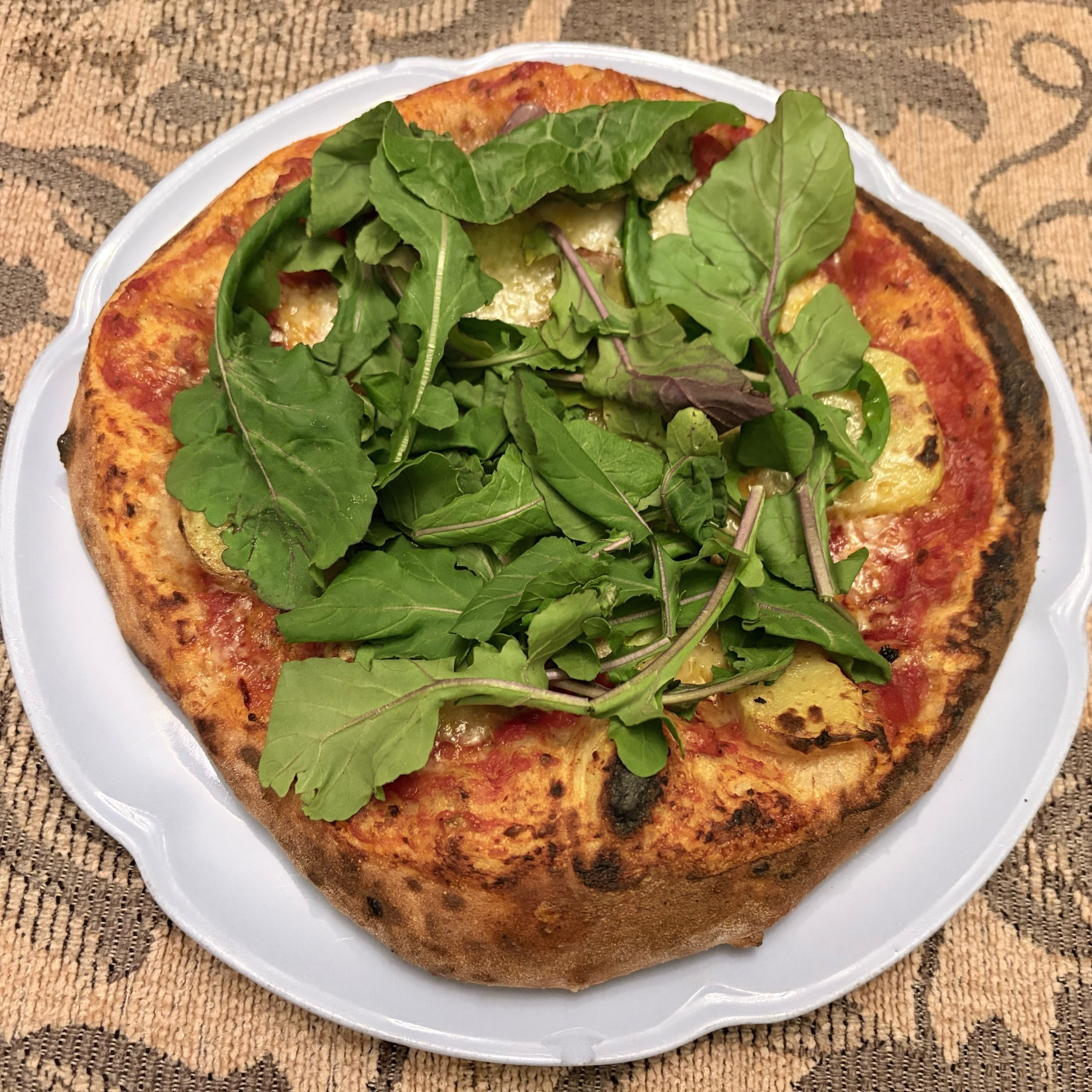 Close up view of a small pizza covered in arugula sitting on a pale blue plate set on a light brown tablecloth.