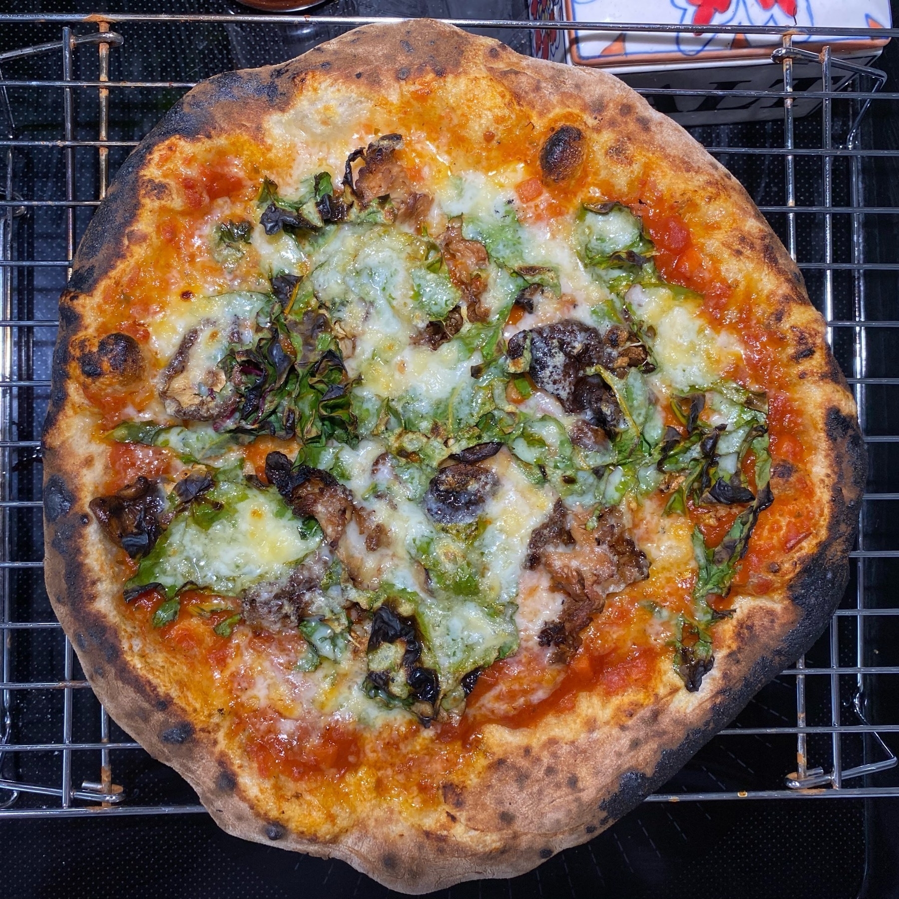 Small pizza on a cooling rack sitting on a black stove top.