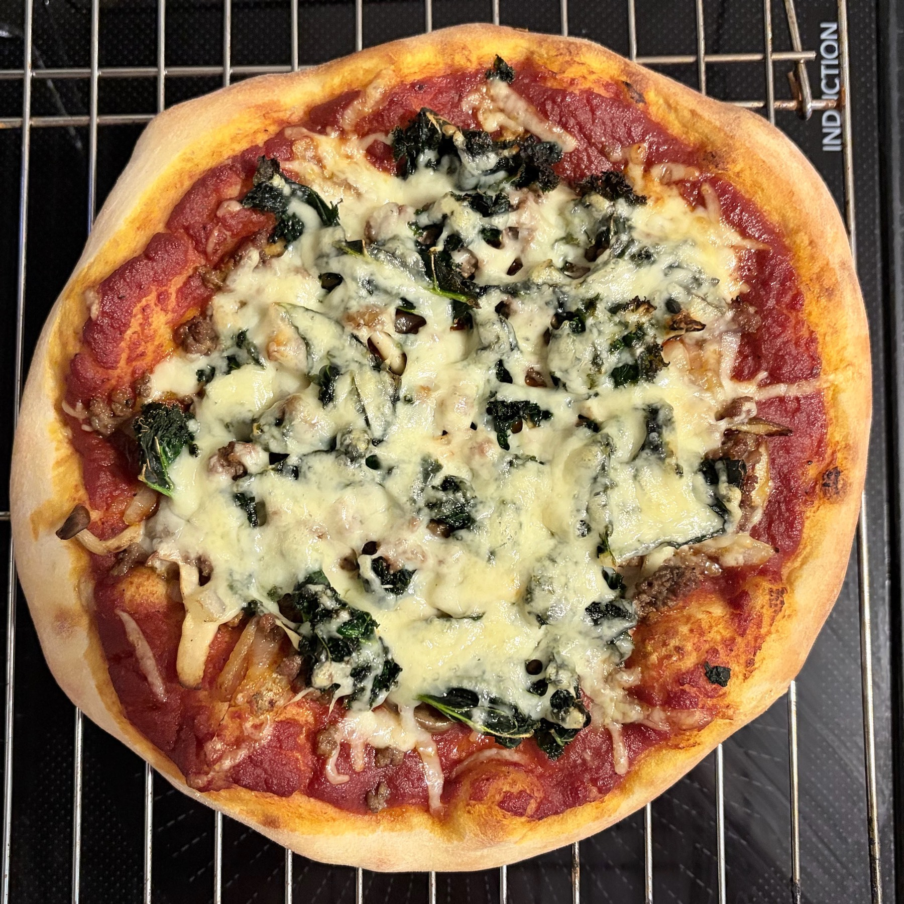 A small pizza on a cooling rack, sitting on top of a black induction stove top.