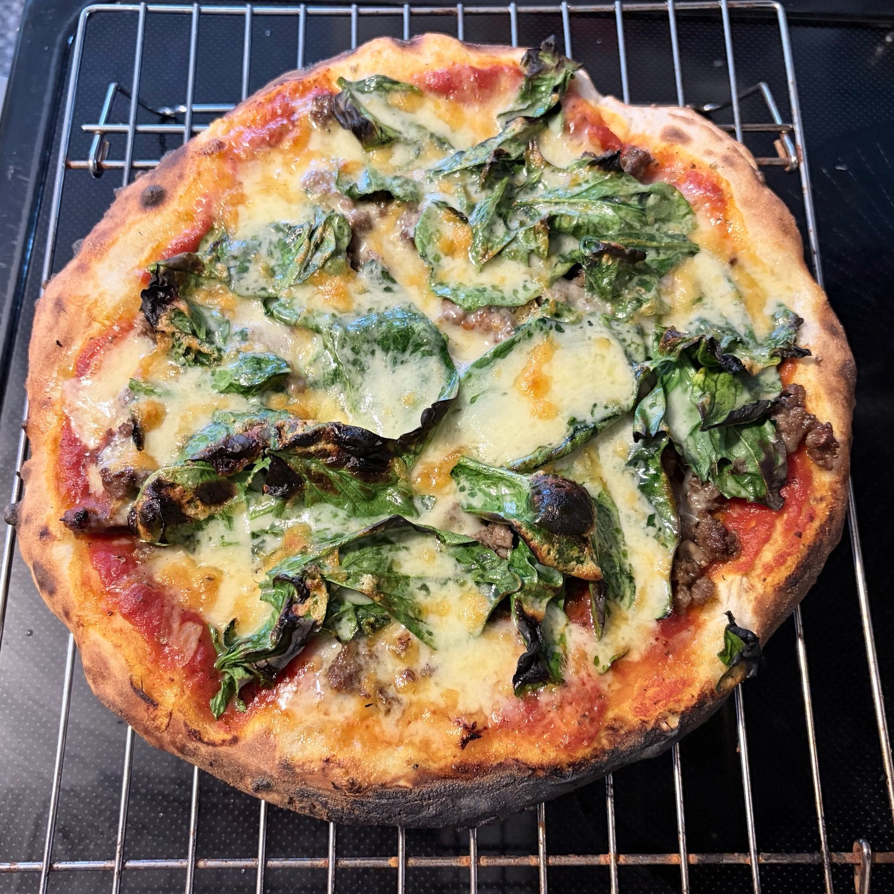 Small pizza on a metal cooling rack, sitting on a black glass cooking surface.