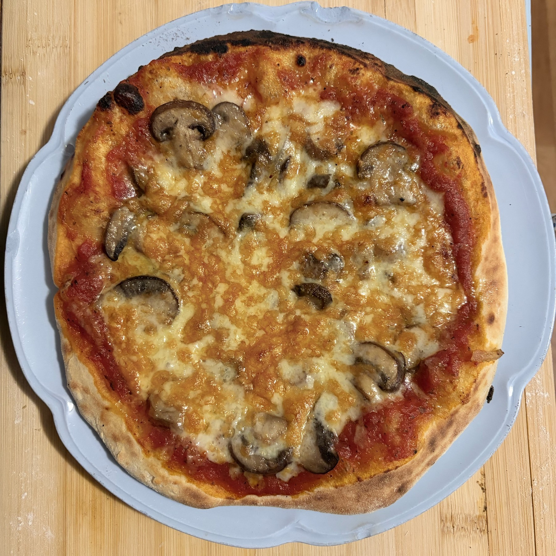 Small pizza on a blue plate, sitting on a wooden cutting board, seen from above.