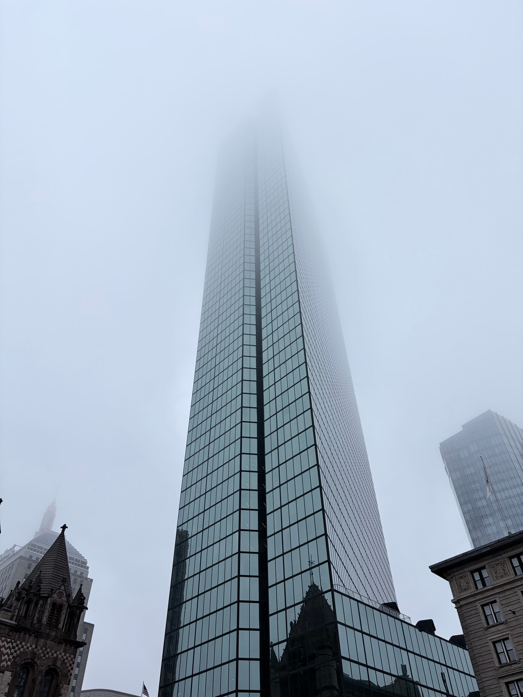 View of the 200 Clarendon St office tower in Boston from below on a foggy day, with the top of the windowed skyscraper vanishing into the haze above.