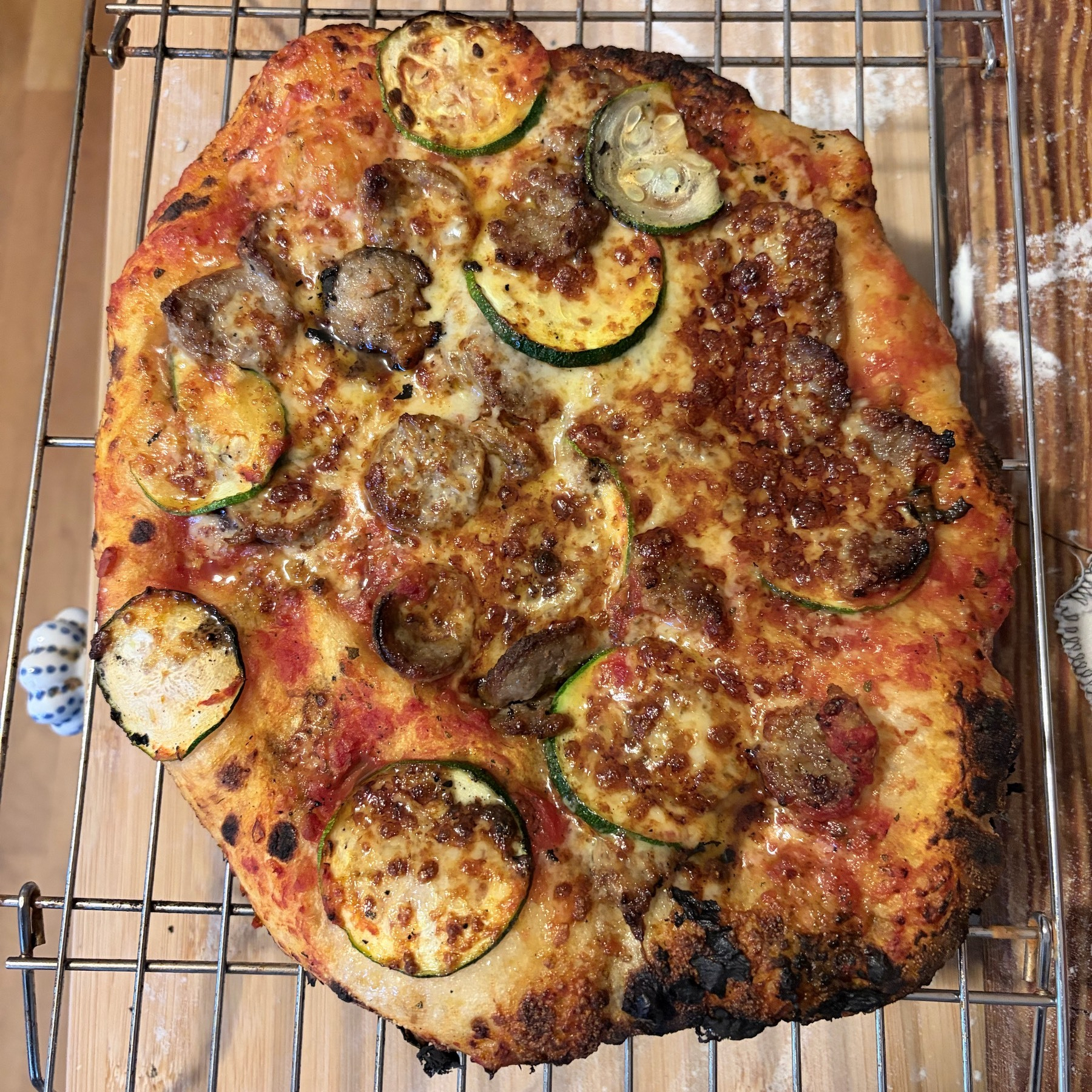 Small pizza on a cooling rack sitting on a wooden cutting board. 