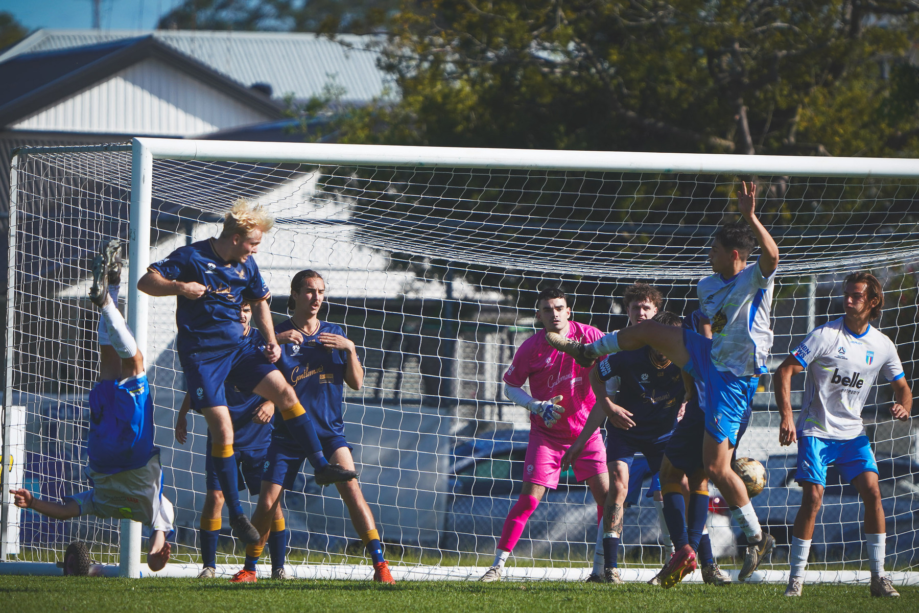 A group of soccer players are actively competing near the goal during a match, with some players attempting to score and others defending.