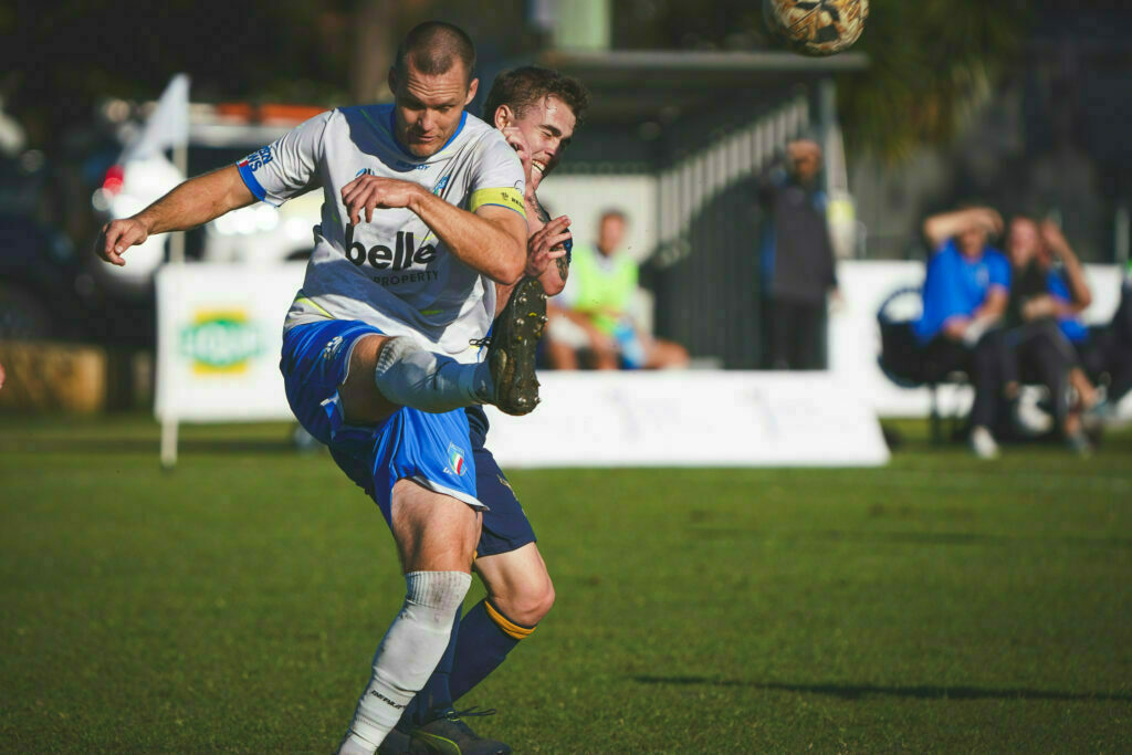 Two soccer players are competing for the ball on a grassy field during a match.