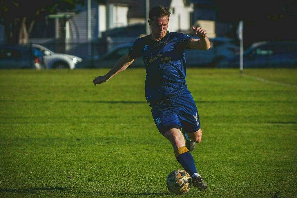 A soccer player in blue attire is kicking a ball on a grassy field.