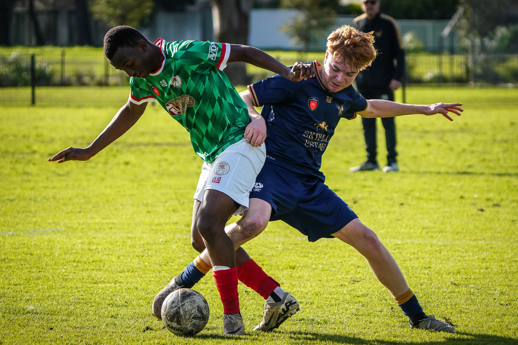 Two soccer players compete for the ball on a grassy field.