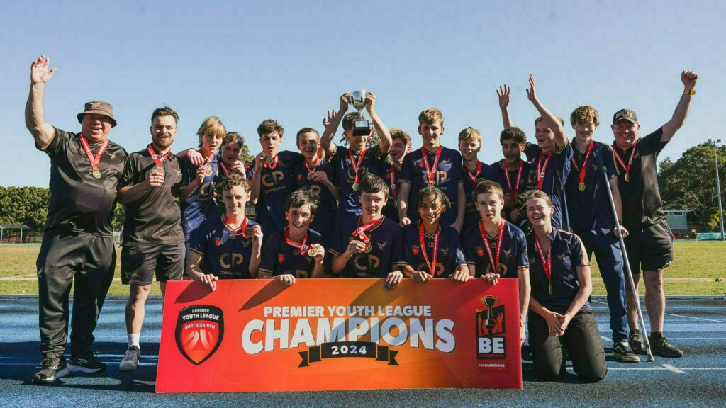 A youth sports team celebrates their championship win outdoors, holding a trophy and a Premier Youth League Champions 2024 banner.