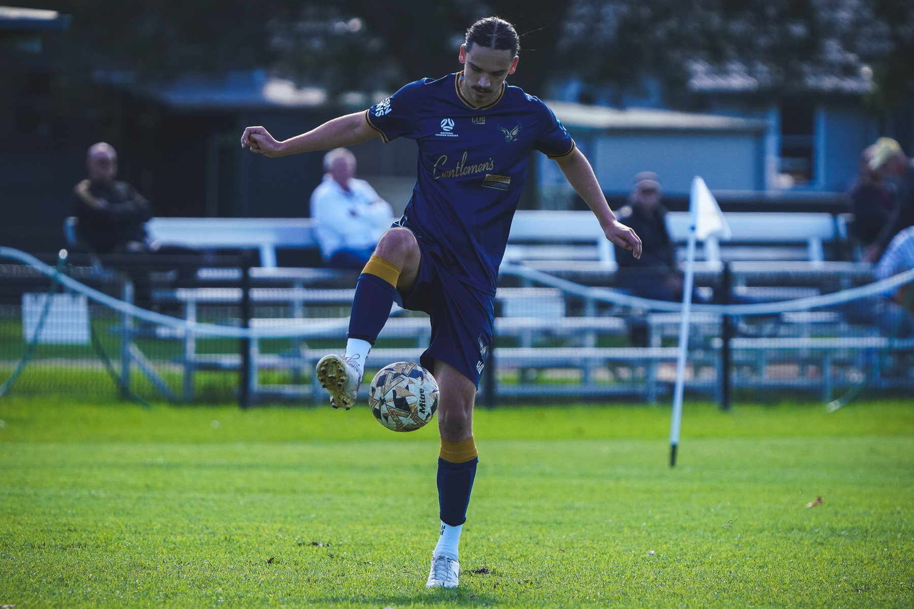 A soccer player in a blue uniform is controlling the ball with his foot on a grassy field.