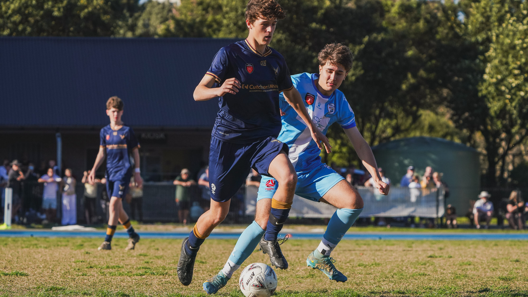 Two soccer players compete for the ball on a grassy field during a match.