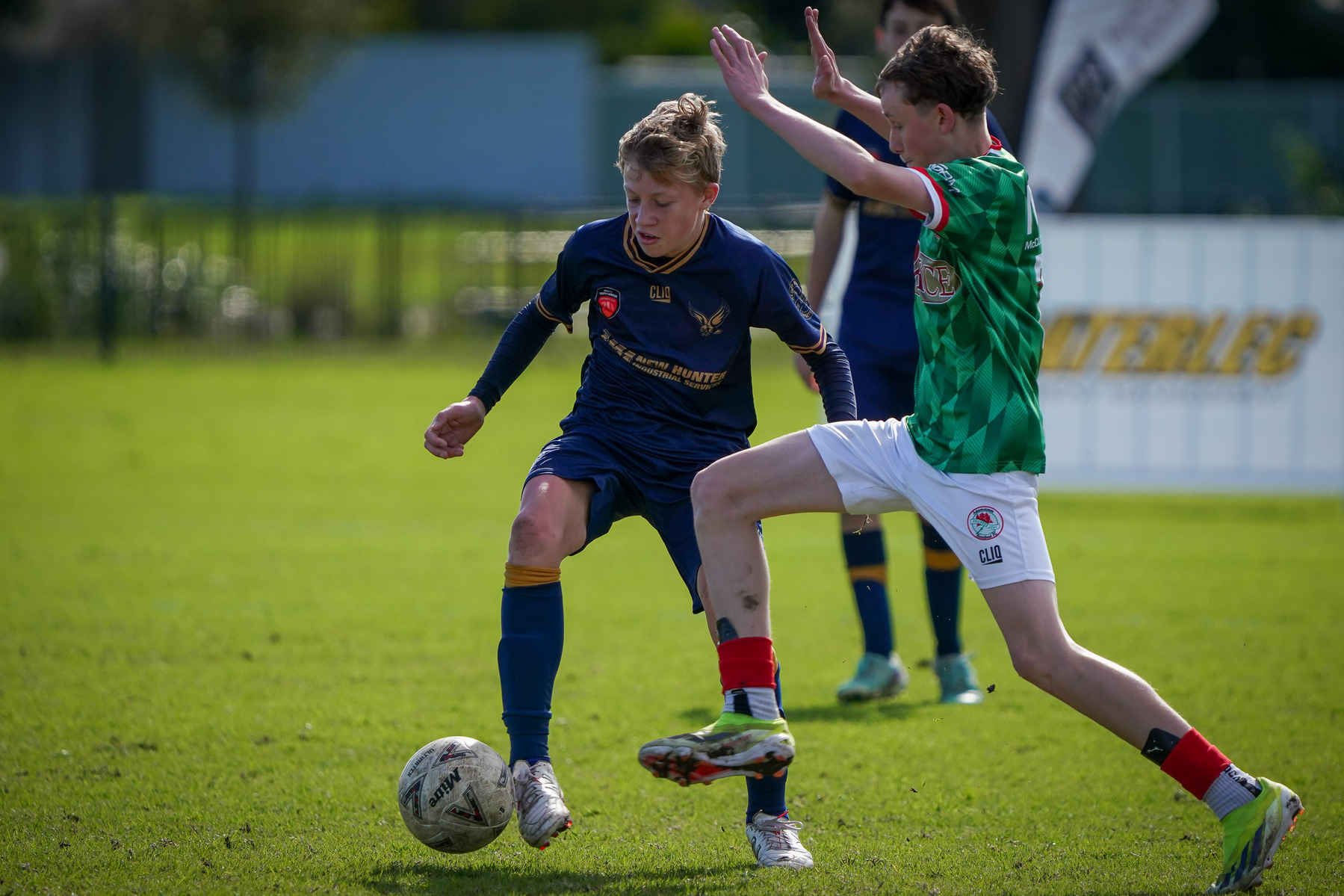 Two youth soccer players compete for the ball on a grassy field during a game.