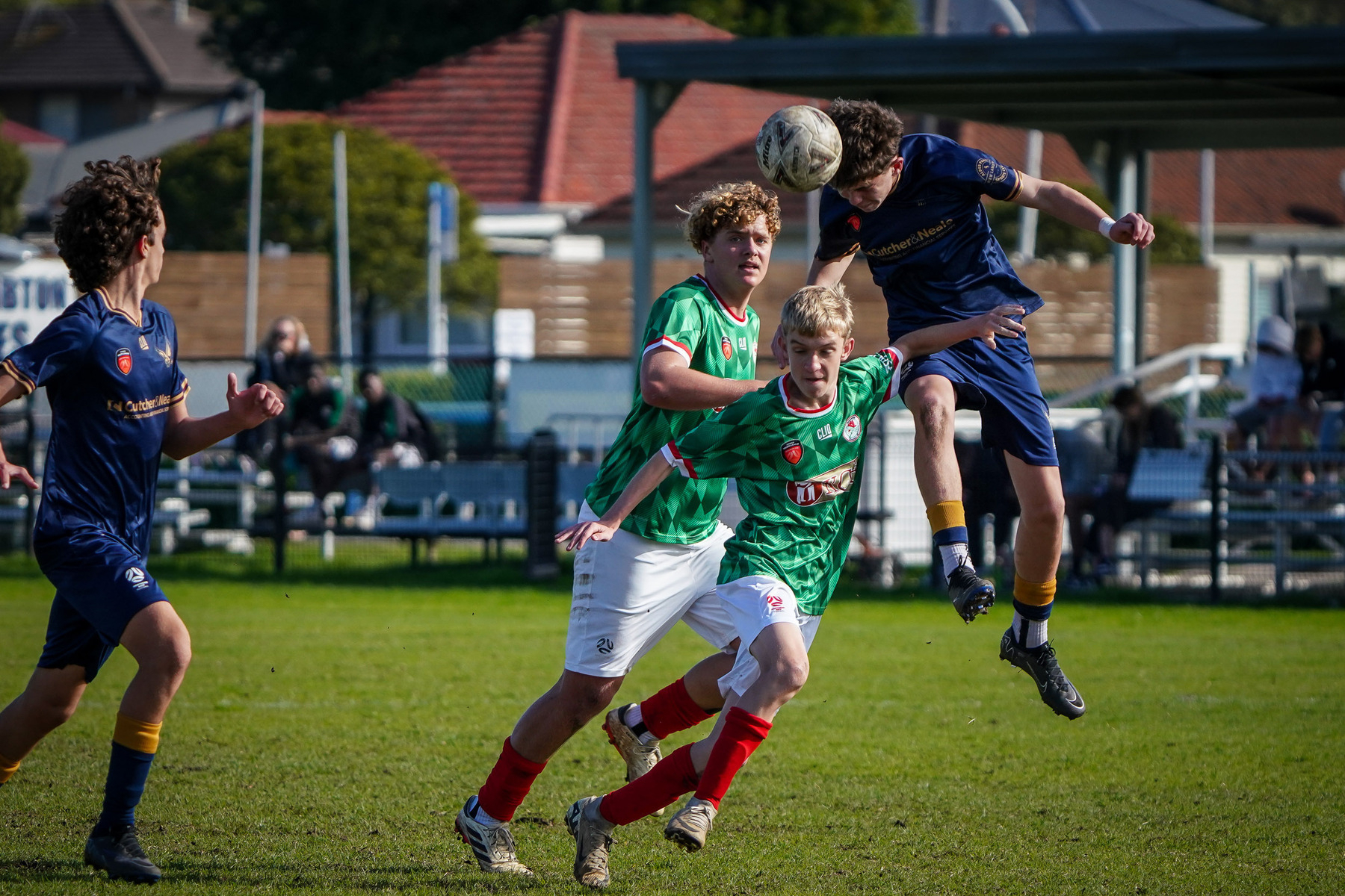 Four soccer players on a field compete for a header during a match.