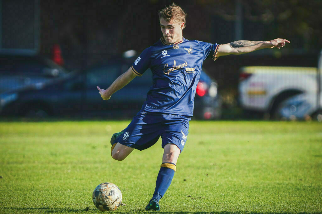 A soccer player in a blue uniform is preparing to kick a ball on a grassy field.