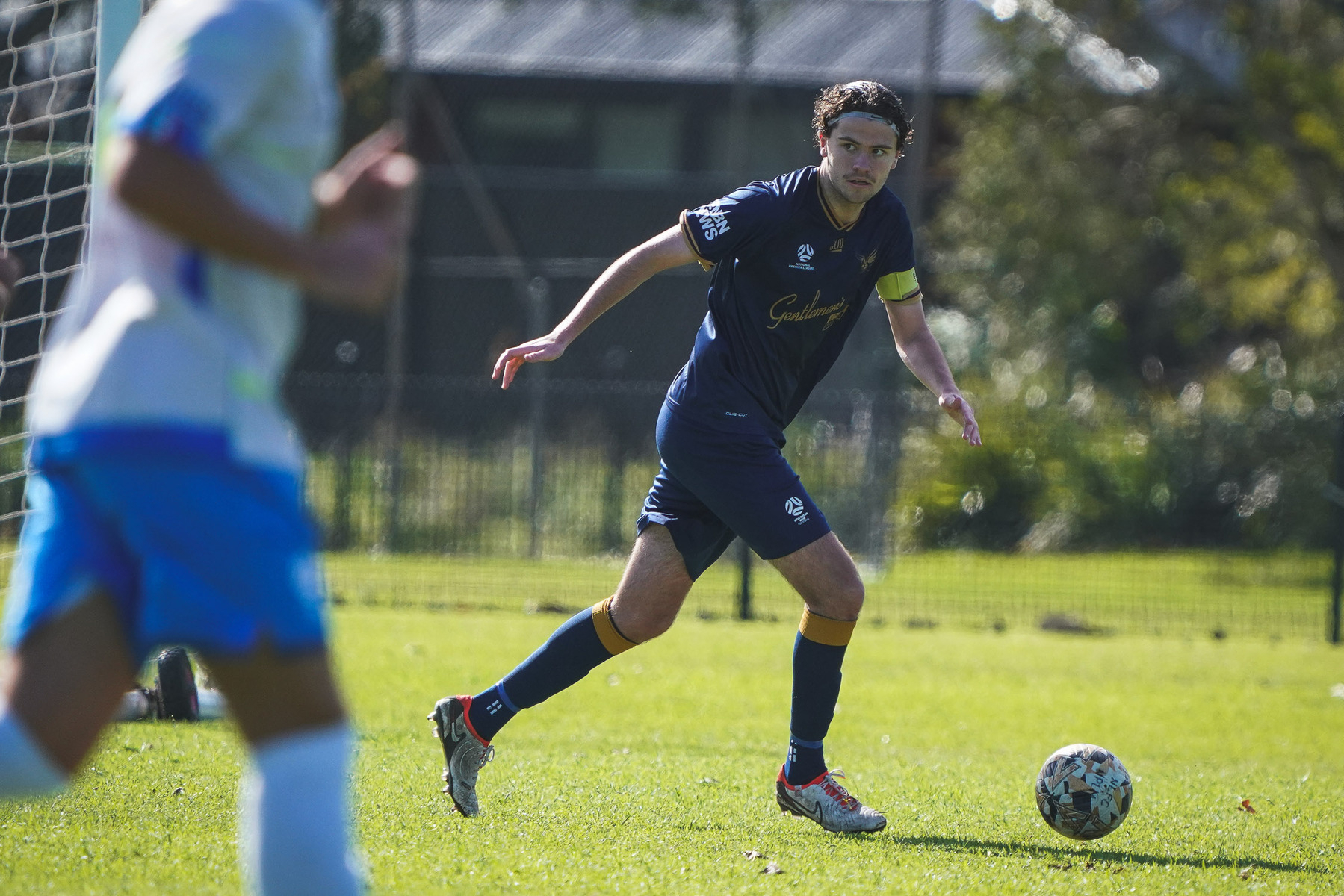 A soccer player wearing a navy blue kit is about to kick the ball during a game on a grassy field.