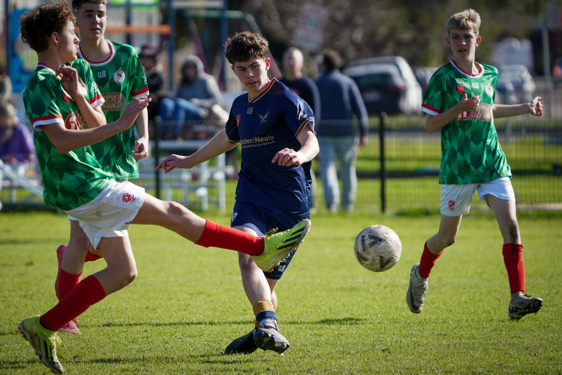 A group of boys are playing soccer on a grassy field, with one player in blue actively kicking the ball.