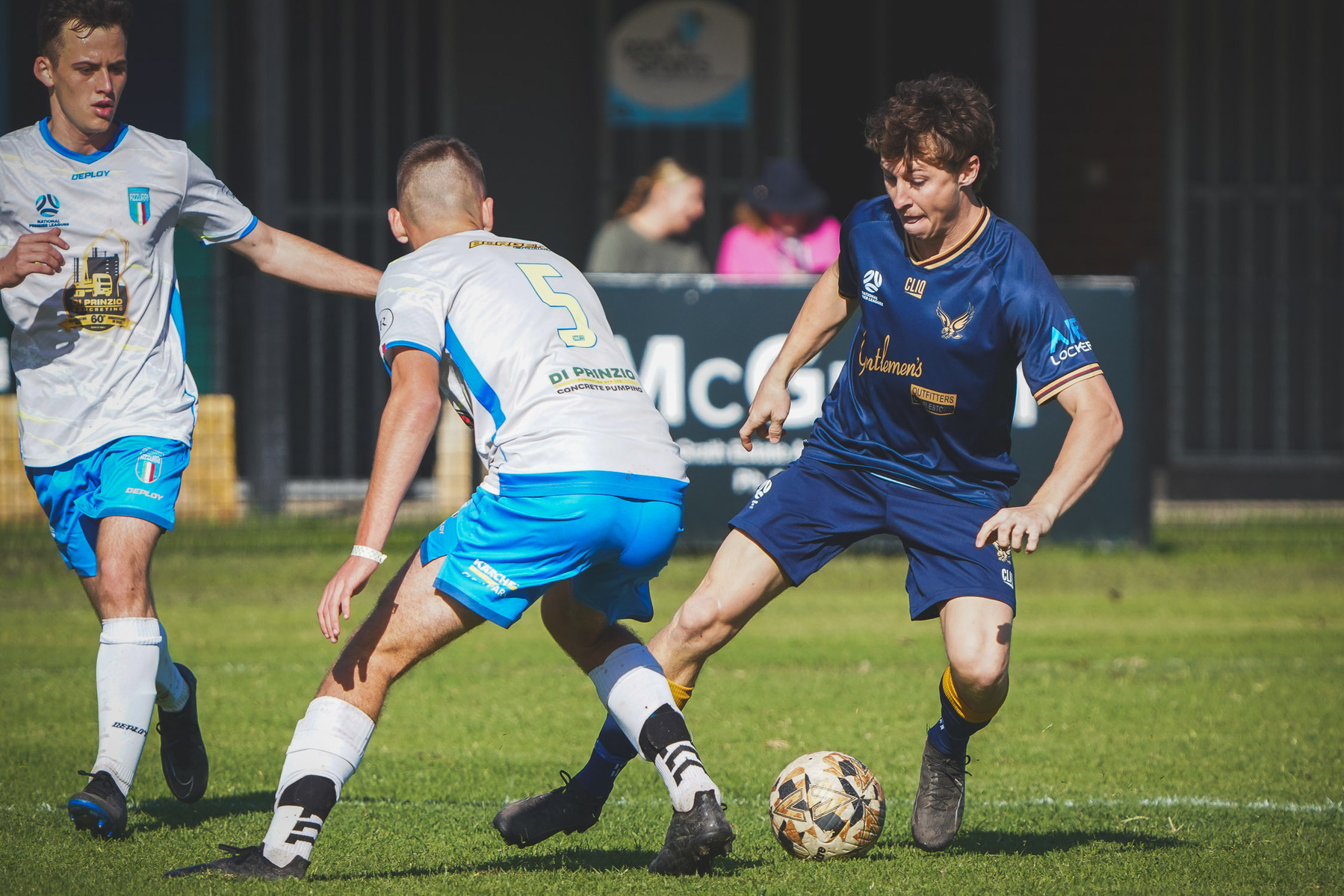 Two soccer players are competing for the ball on a grassy field, with another player nearby.