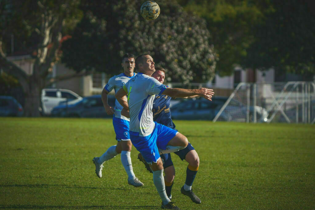 Two soccer players are competing for a ball in mid-air on a grassy field.