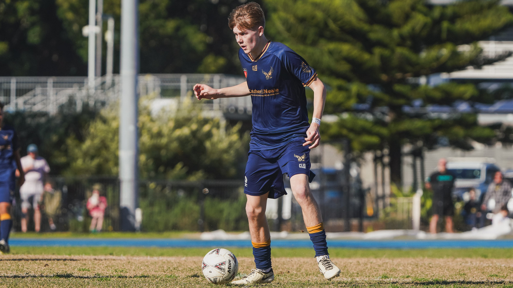 A soccer player in a navy blue uniform dribbles a ball on a grassy field.