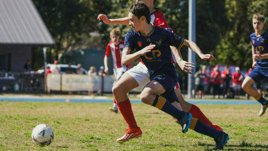 A soccer player in a navy uniform is swiftly maneuvering the ball past opponents on a grassy field during a match.