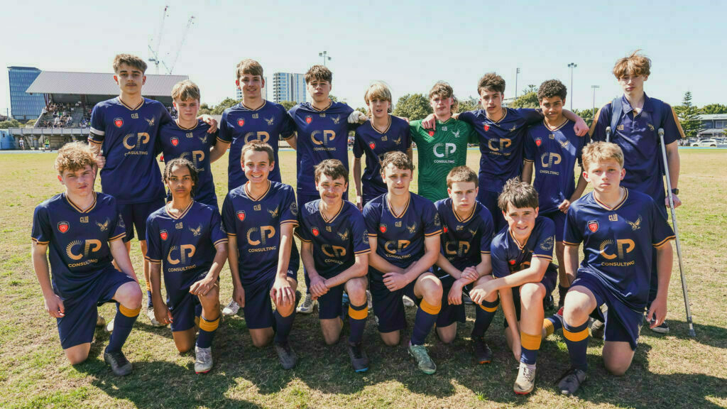 A group of young soccer players in matching uniforms poses together on a grassy field.