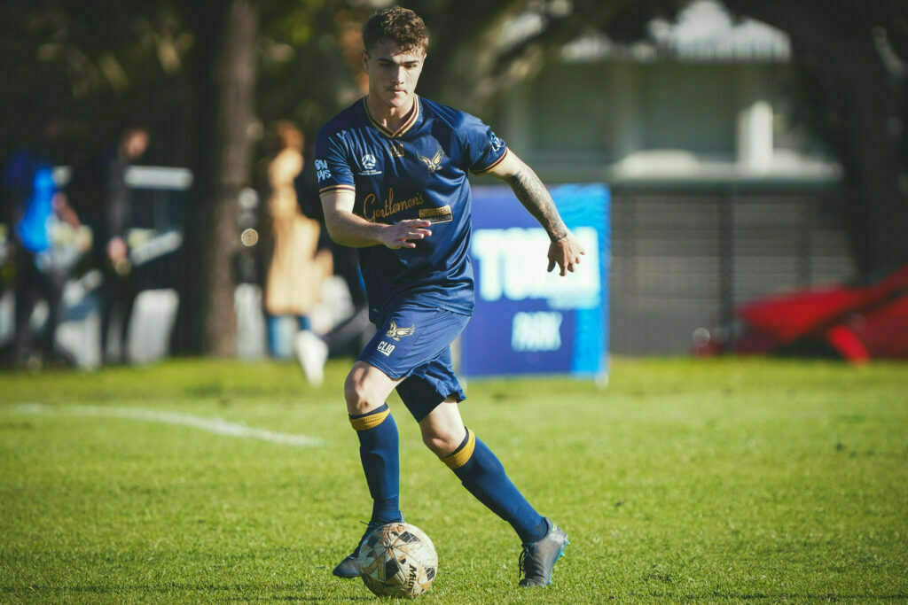 A soccer player in a blue uniform is dribbling a ball on a grassy field during a match.