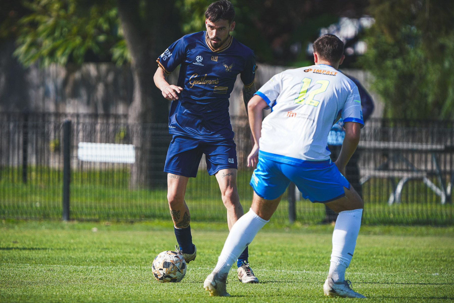 Two soccer players are engaged in a match, one wearing a blue uniform and the other in a white one, on a grassy field.