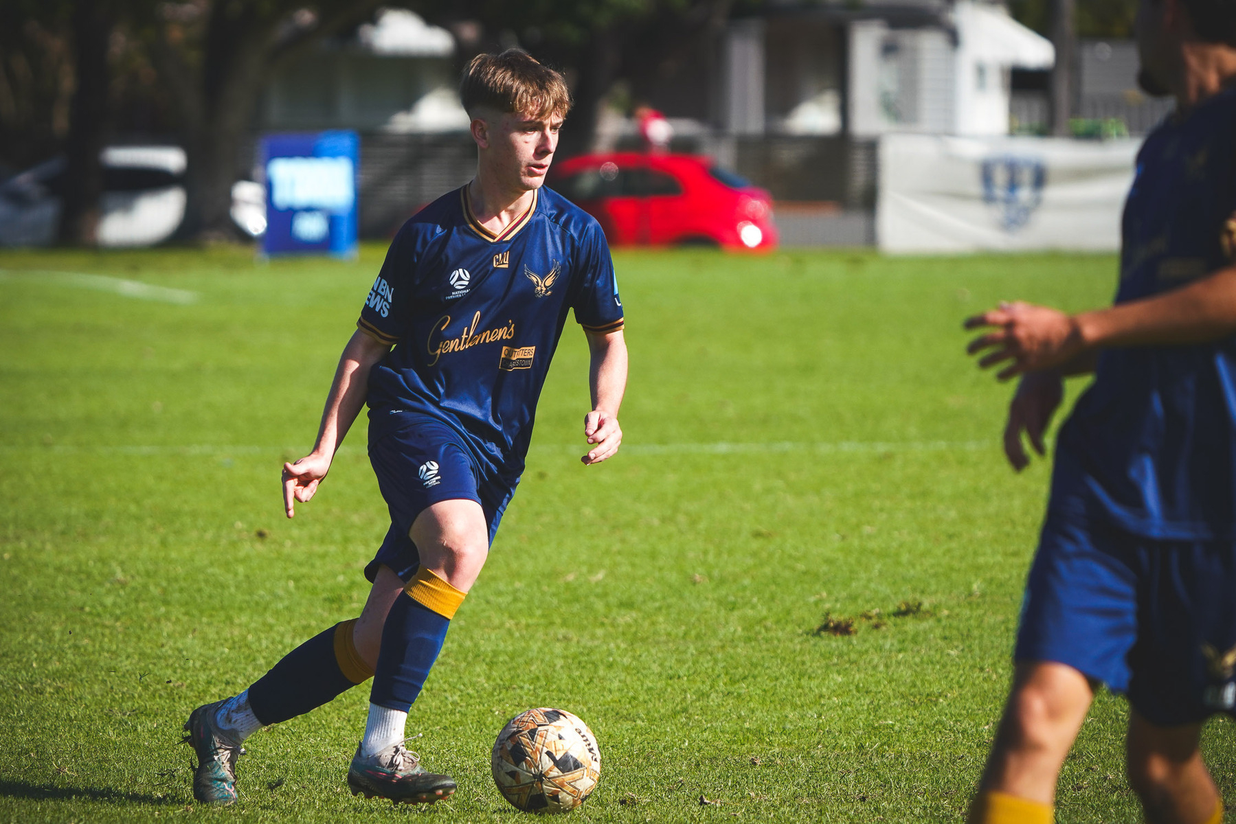 A soccer player in a blue uniform is dribbling the ball on a grassy field.