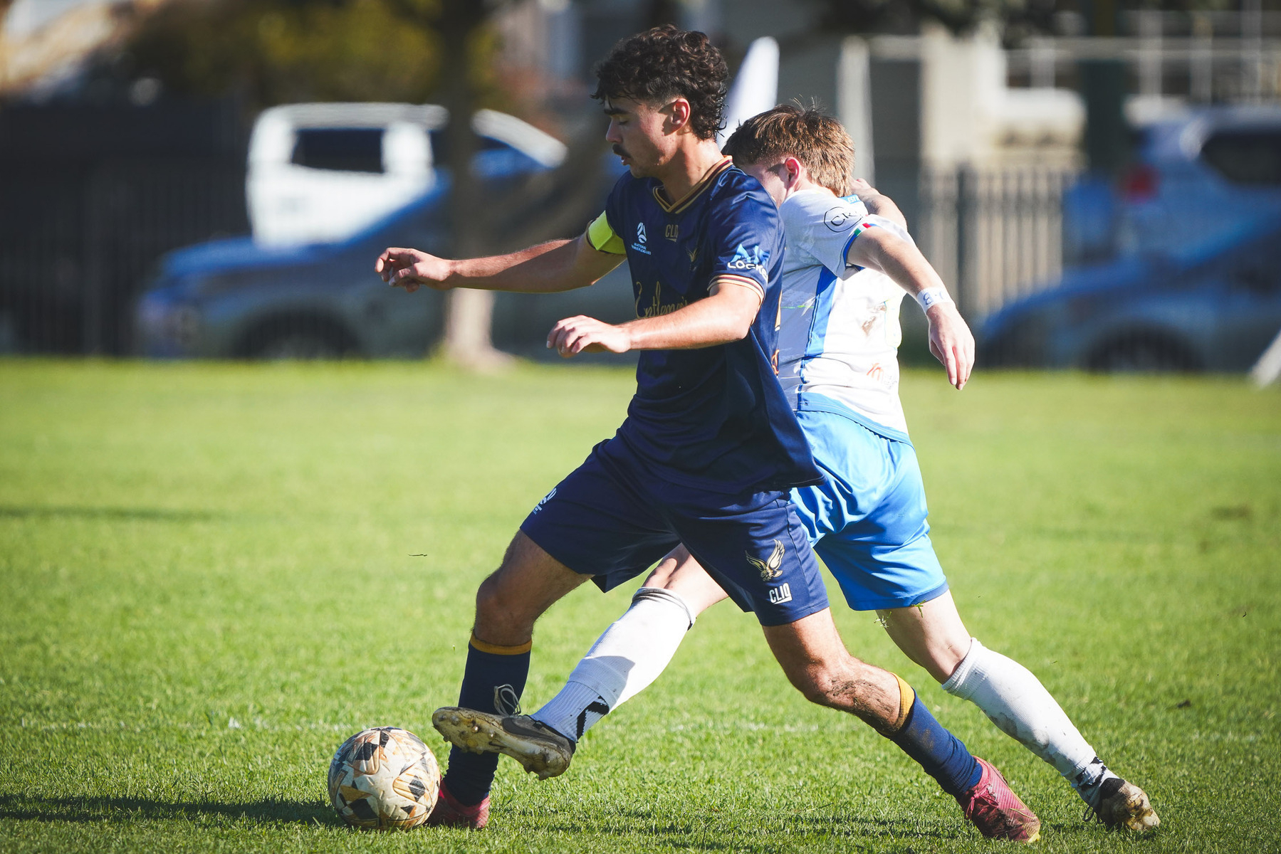 Two soccer players are competing for the ball on a grassy field.