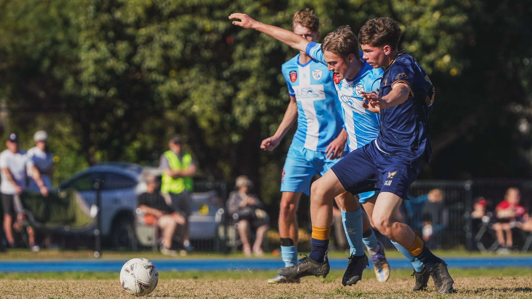 Two soccer players in blue uniforms are competing for the ball during a daytime match.