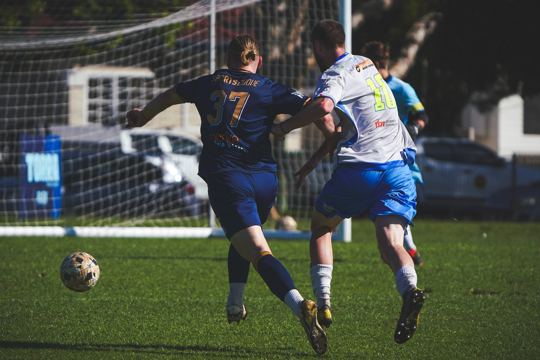 Two soccer players in blue and white jerseys are competing for the ball on a grassy field.