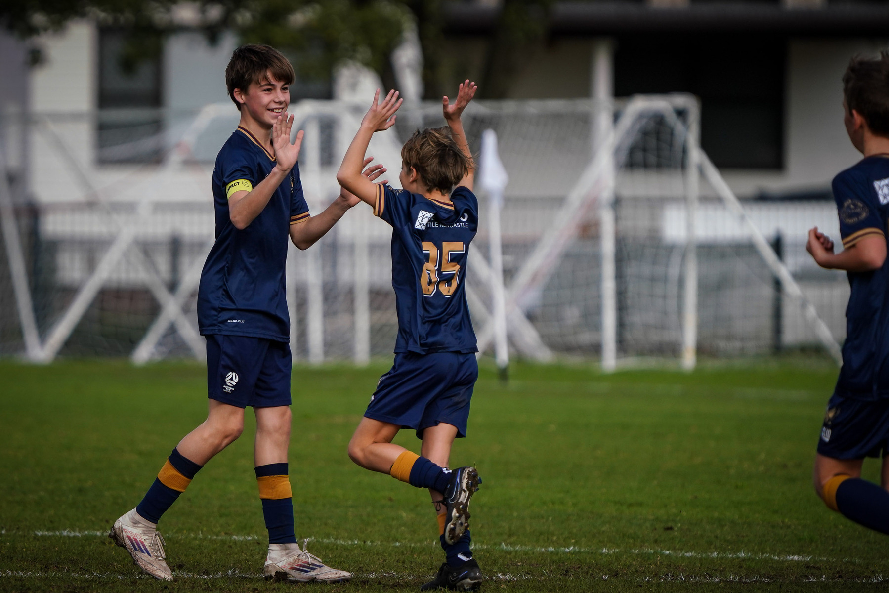 Two young soccer players in blue uniforms celebrate with high-fives on a grassy field.