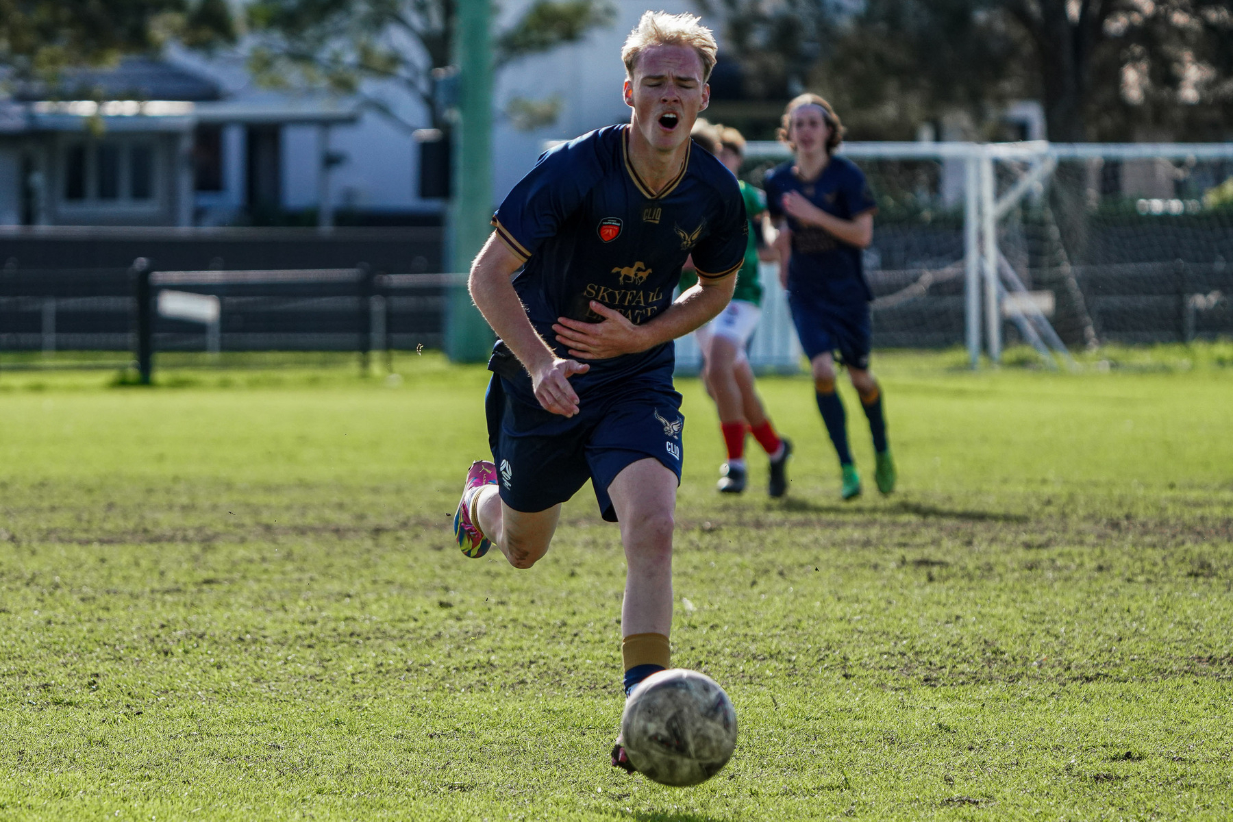 A soccer player in a blue uniform is actively chasing a ball on a grassy field.