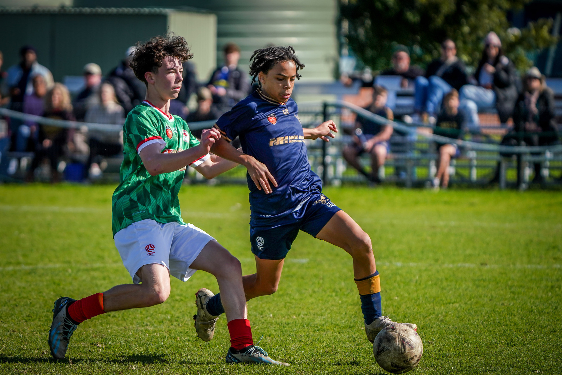 Two soccer players are competing for control of the ball on a grassy field during a match.