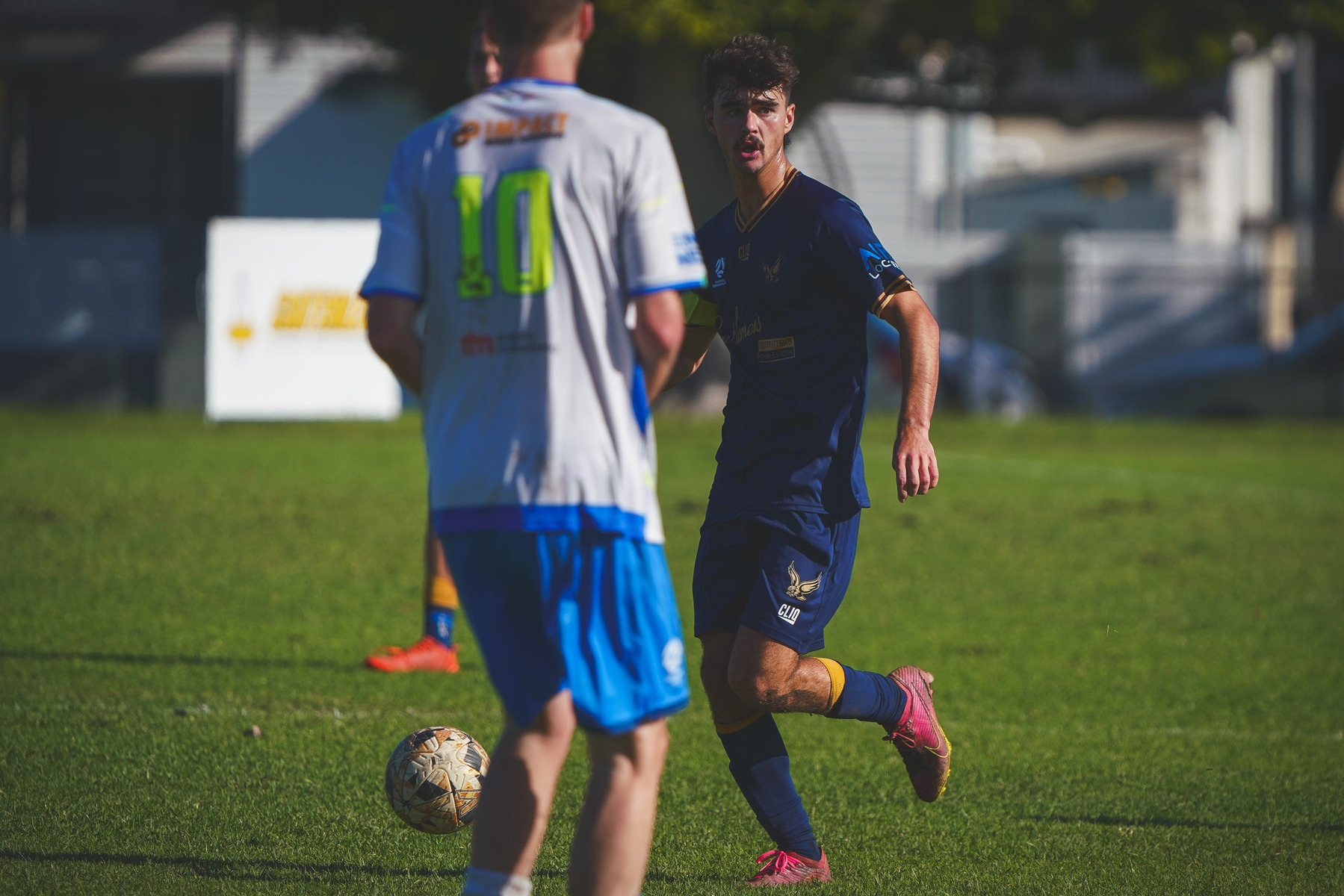 Two soccer players are on a grassy field, with one in a navy uniform and the other in a white and blue uniform.