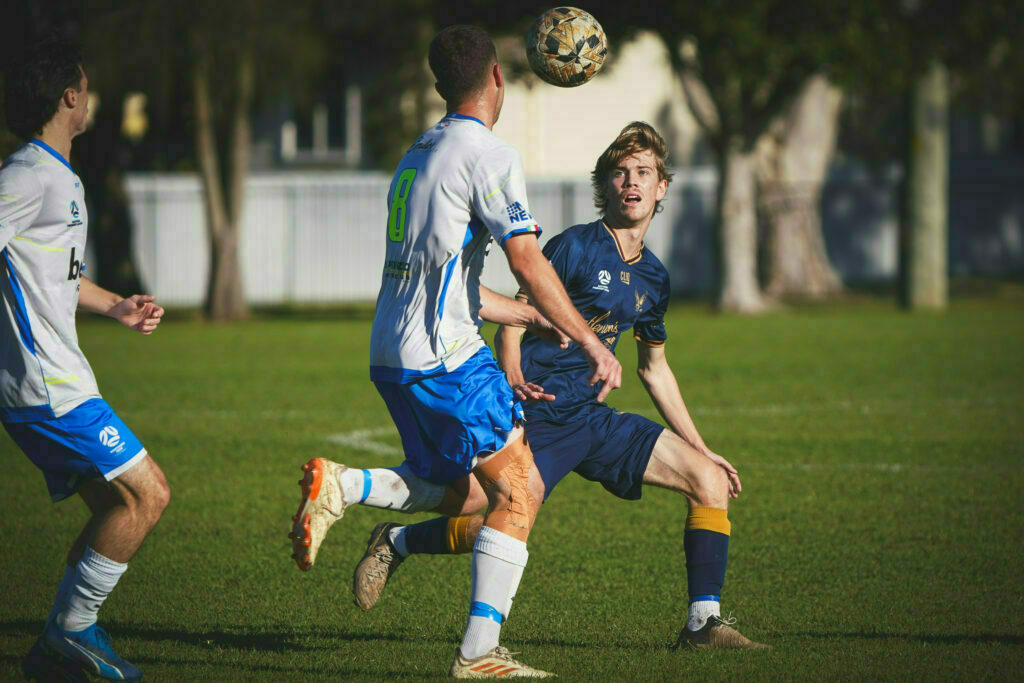 Two soccer players are competing for the ball on a grassy field, with one player attempting a kick and the other watching intently.