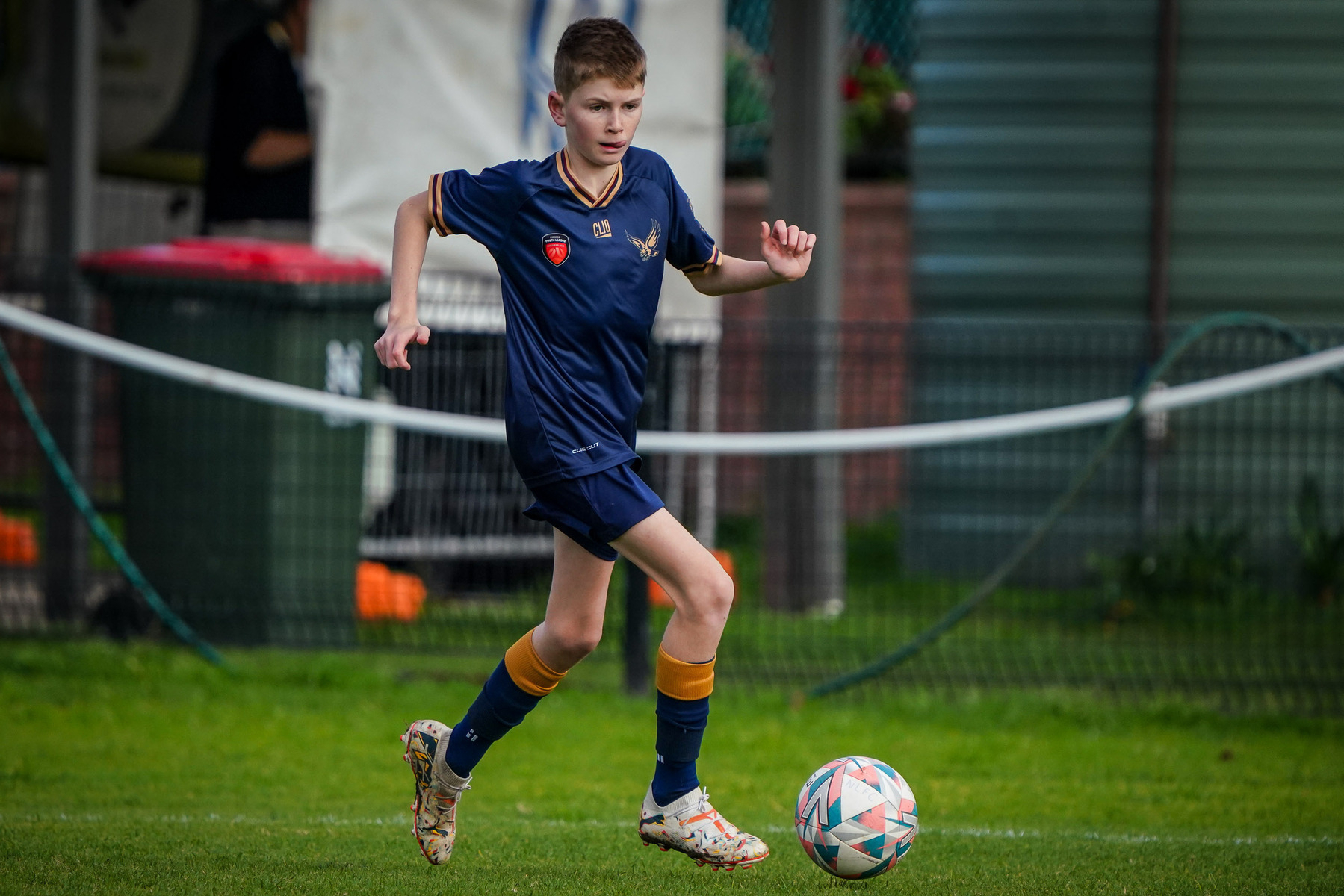 A young soccer player in a navy-blue uniform is running with a ball on a green field.