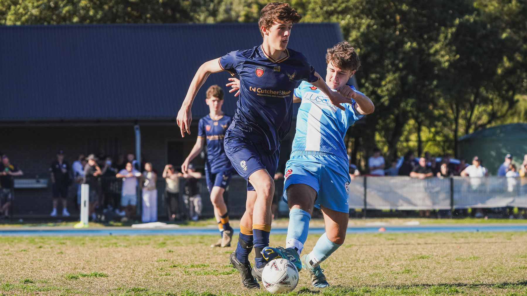 Two young soccer players are competing for the ball on a field during a match.