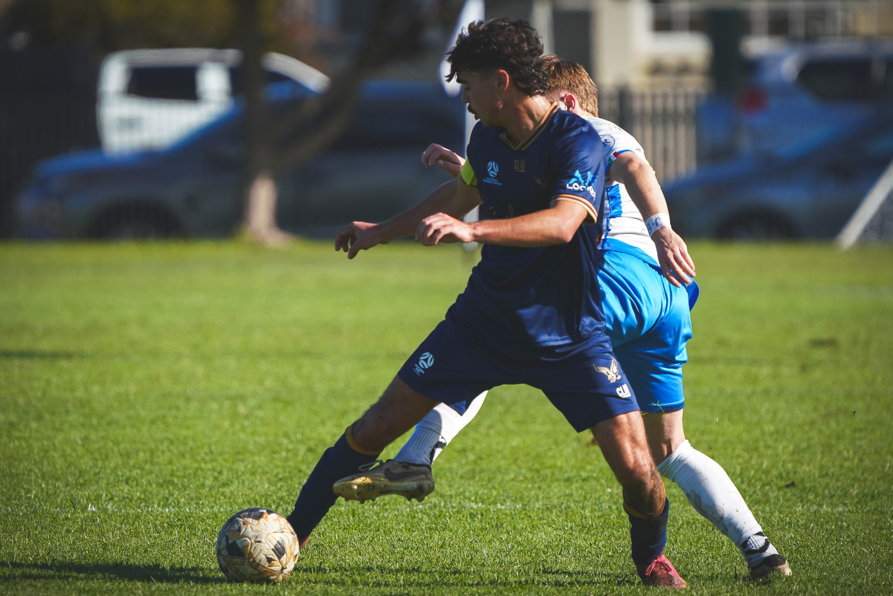 Two soccer players are competing for the ball on a grassy field.