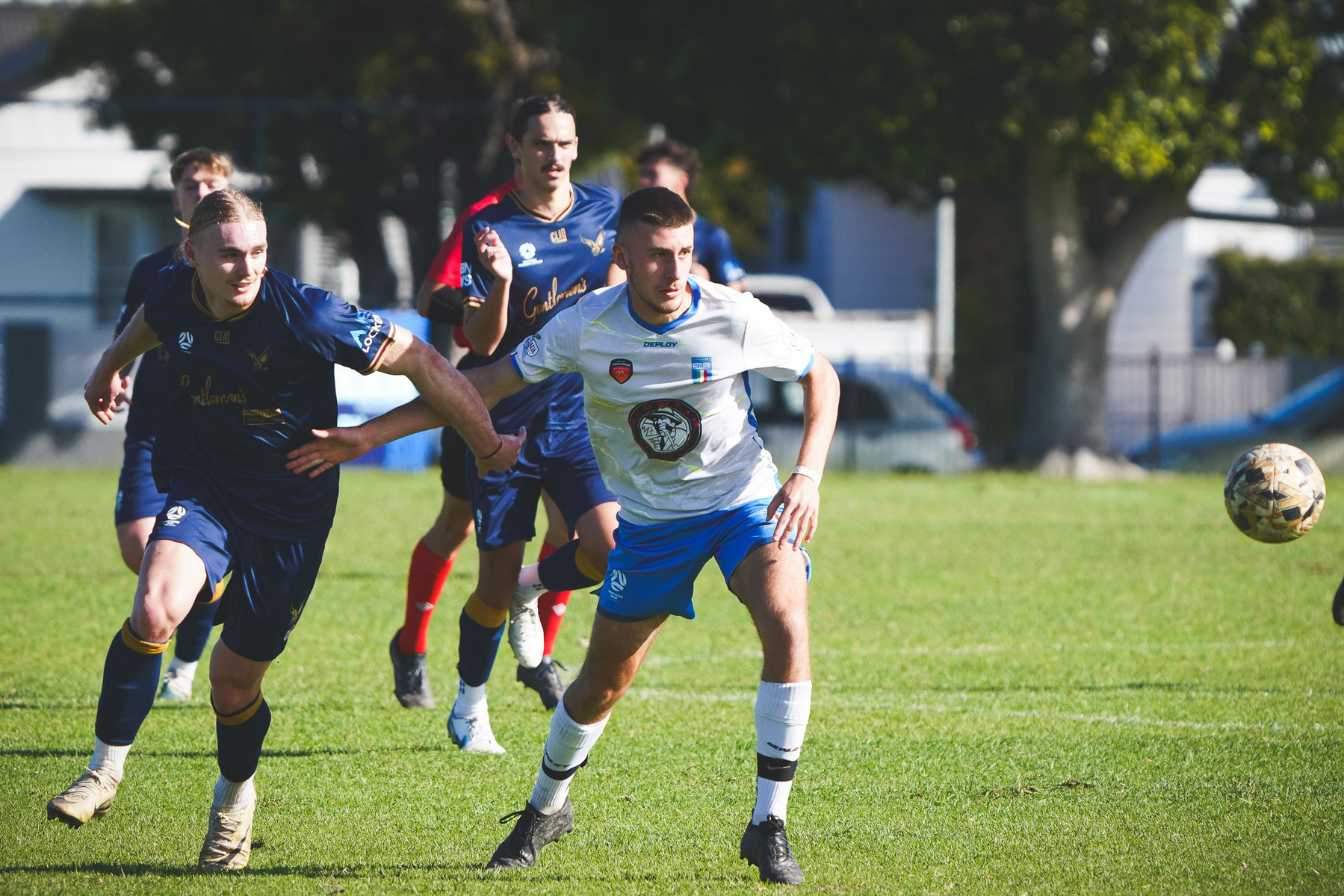 A group of soccer players is actively engaged in a match, with one player in blue and another in white focused on the ball.