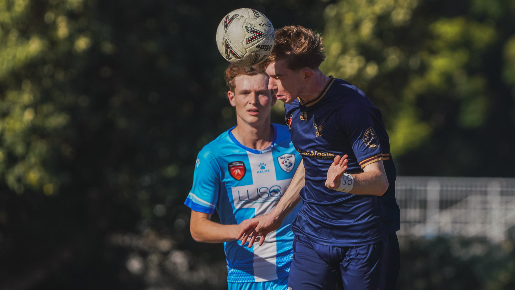 Two soccer players vie for the ball in mid-air during a match.