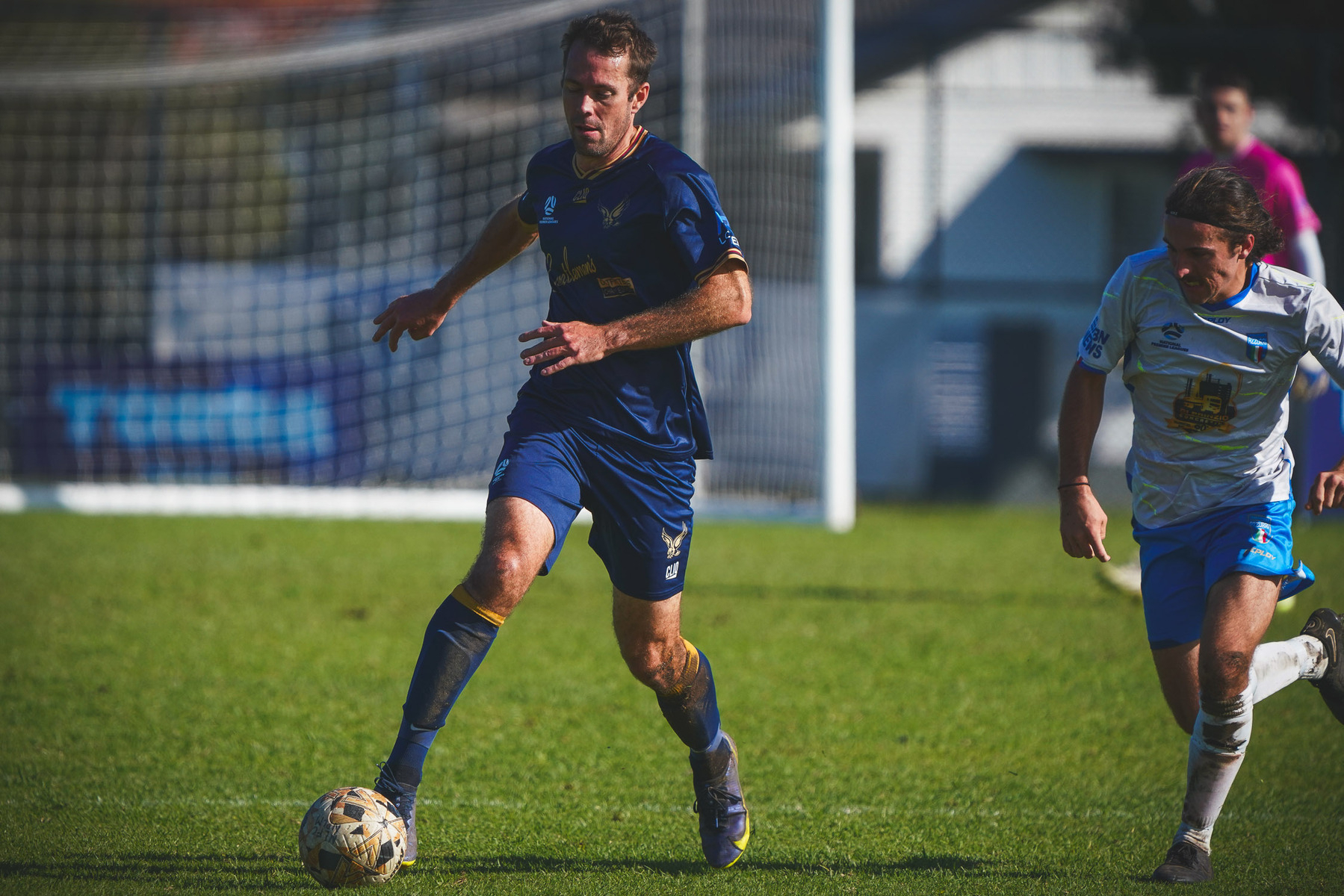 Two soccer players are in action on the field, with one dribbling the ball while the other chases.