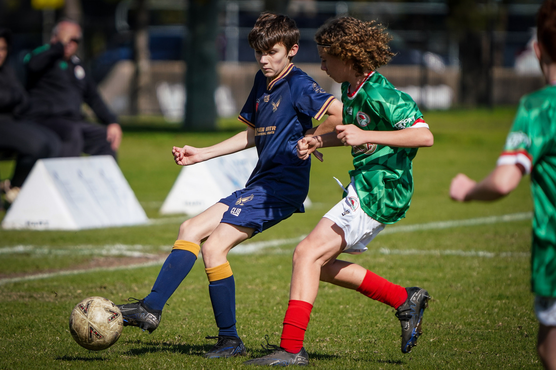 Two young soccer players are competing for control of the ball on a grassy field during a match.