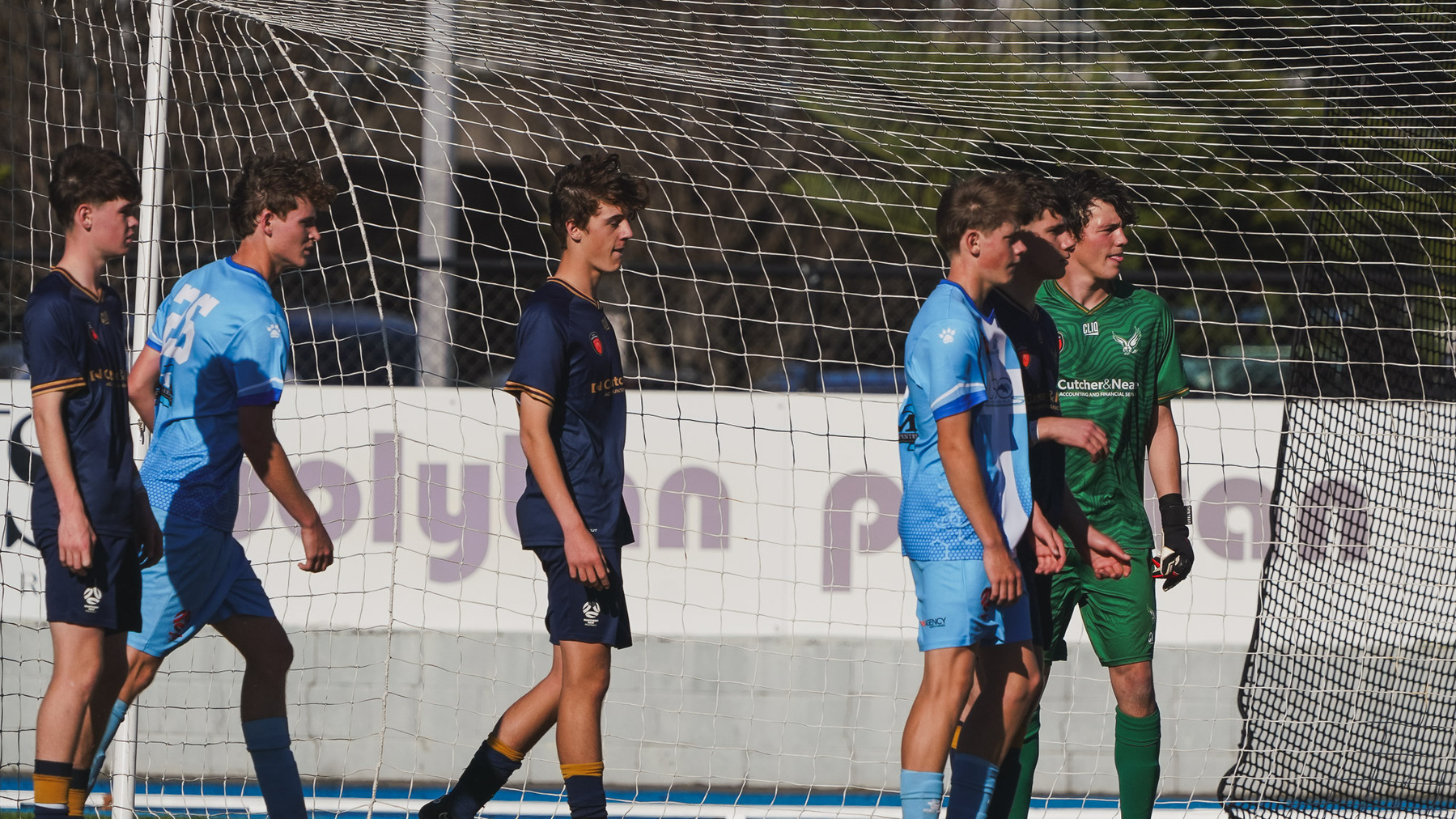 A group of soccer players, wearing different colored uniforms, are gathered near the goalpost during a game.