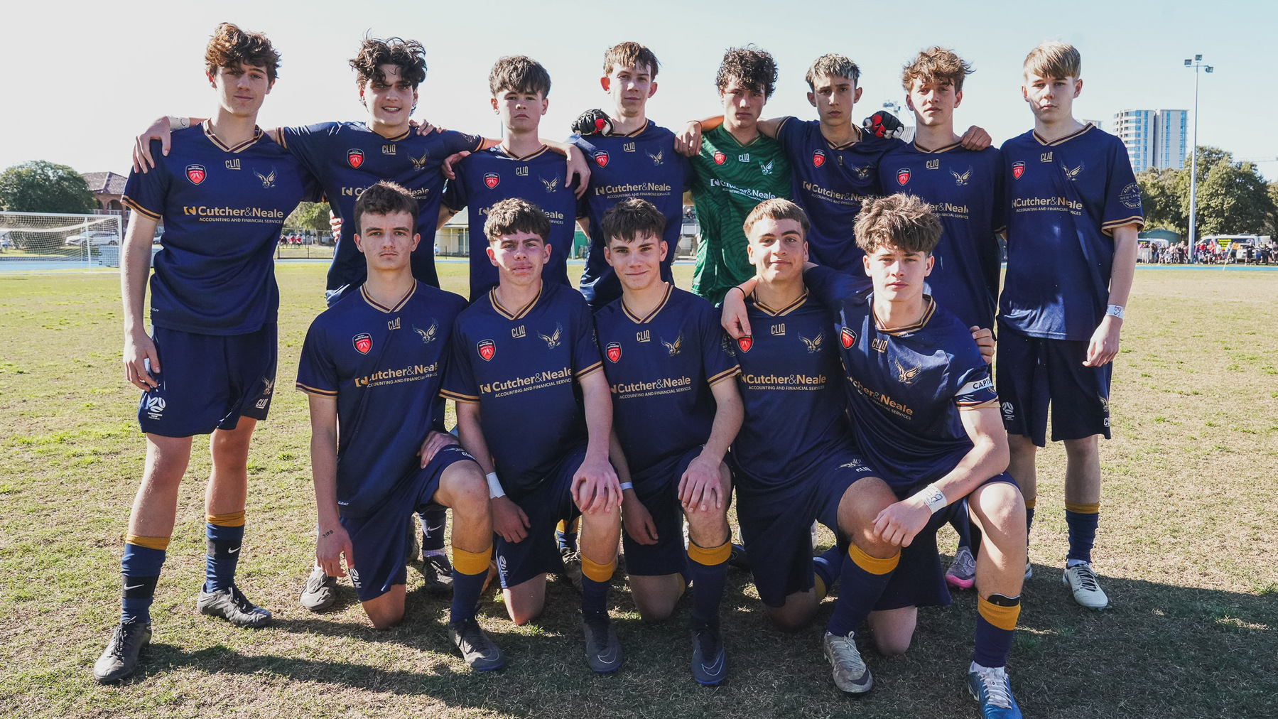 A group of young soccer players in blue uniforms pose together on a field.