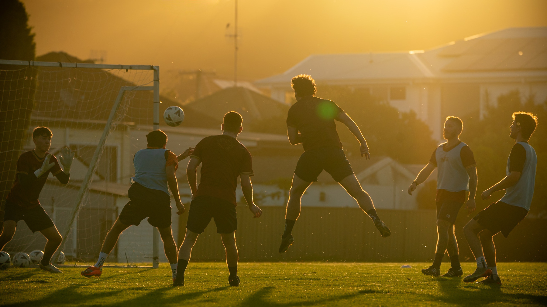 A group of people are playing soccer during sunset.